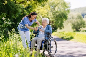 Life Assure Senior Woman In Wheelchair With Caregiver At Park Hero